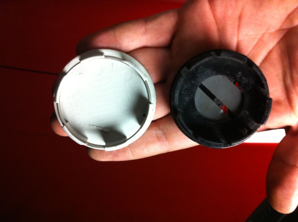 Two wheel center caps, one white and one black, held in a hand over a red surface