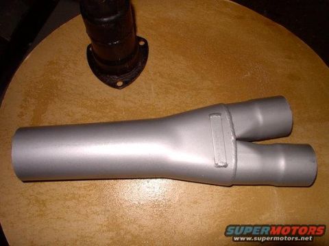 1982 Ford Bronco - Exhaust Y-pipe shown on a wooden surface. A portion of a black exhaust pipe is also visible.