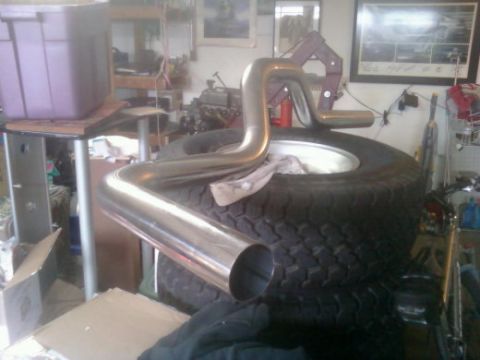 1982 Ford Bronco - A shiny exhaust pipe is placed on top of stacked tires in a cluttered garage setting.