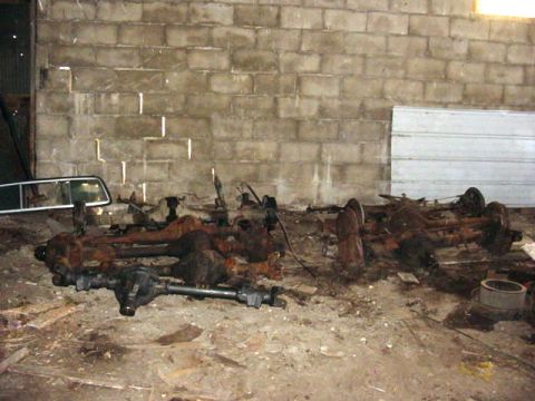 1992 Ford Bronco - Multiple vehicle axles are piled on the floor of a workshop, with a cinder block wall in the background.