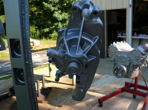 1976 Chevrolet Corvette - A painted engine part hangs in front of a V8 engine on a stand, with a garage and trees visible.