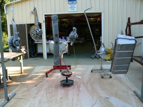 1976 Chevrolet Corvette - Various car parts, including a fuel tank and suspension components, are suspended or mounted on stands for painting outside a workshop.
