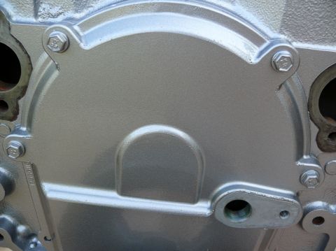 1976 Chevrolet Corvette - A close-up view of a silver-painted engine timing cover, showing bolted edges and a distinctive raised semi-circular detail.