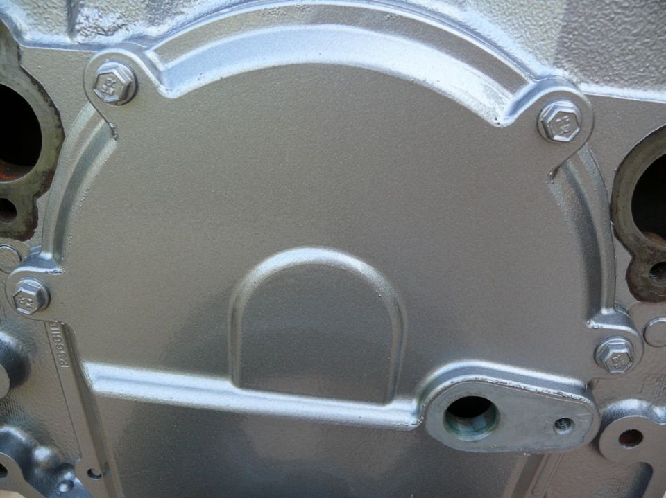 Close-up of a silver engine timing cover with bolts and a small raised semi-circle detail
