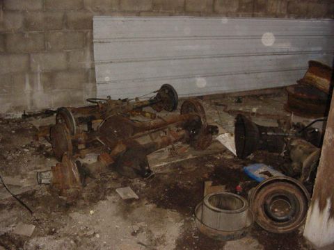1992 Ford Bronco - Several old, rusty vehicle axles are stored in a cluttered garage space.