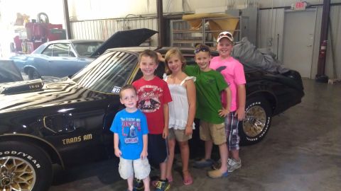1973 Chevrolet Camaro - A group of children stand in front of a black Pontiac Trans Am, with another car visible in the garage behind them.