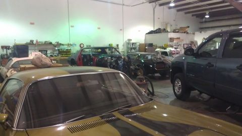 1973 Chevrolet Camaro - A garage scene shows multiple vehicles, including a gold car in the foreground and a dark truck on the right.