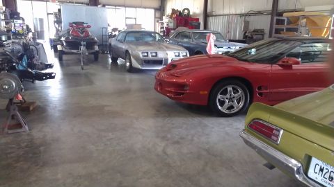1973 Chevrolet Camaro - A red sports car is parked in a garage alongside other vehicles and a jet ski.