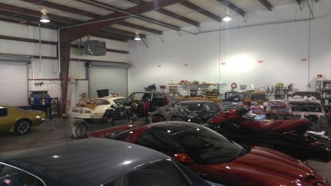 1973 Chevrolet Camaro - Multiple vehicles and jet skis are present inside a cluttered auto repair shop.