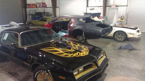 1973 Chevrolet Camaro - Several cars are in a garage, including a black Pontiac Trans Am in the foreground.