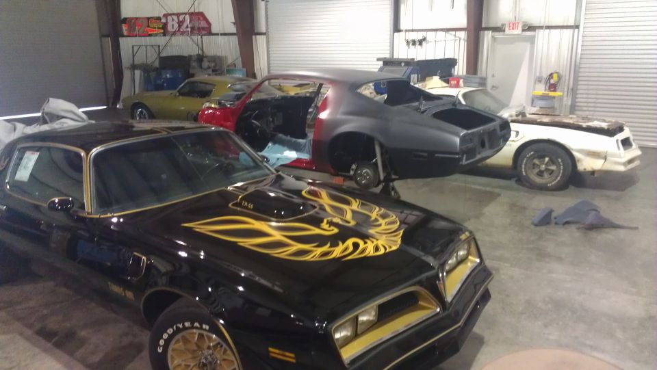 Black Pontiac Firebird Trans Am with gold decals, in a garage with other cars