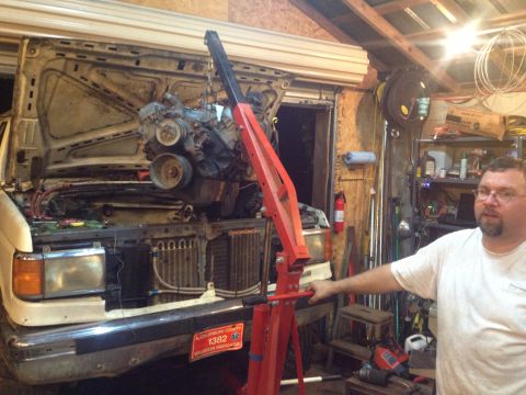 1989 Ford Bronco - Engine hoist is actively removing the engine from a 1989 Ford Bronco in a garage setting.