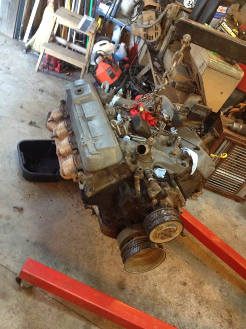 1989 Ford Bronco - Engine assembly resting on an engine stand, surrounded by various garage items and equipment.