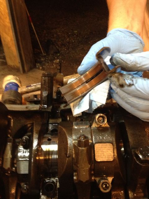 1989 Ford Bronco - Close-up of an engine crankshaft and bearing caps, with a person in gloves holding some of the parts.