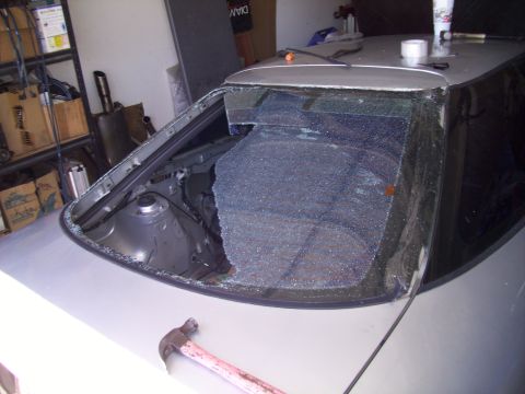 1995 Ford Probe - The rear windshield of a 1995 Ford Probe is heavily damaged, with glass fragments scattered across the interior and exterior.