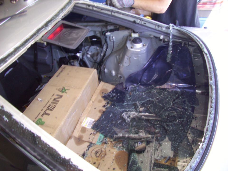 car trunk with shattered rear window, boxes inside, and a person in gloves working