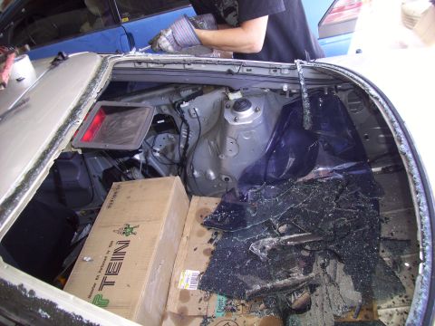1995 Ford Probe - The interior of a car shows a broken rear window and scattered glass, with boxes and a person working on the vehicle.