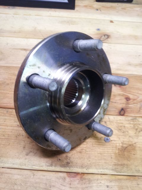 2002 Chrysler 300M - A metal wheel hub assembly is shown resting on a wooden surface, with visible lug bolts and a splined interior.