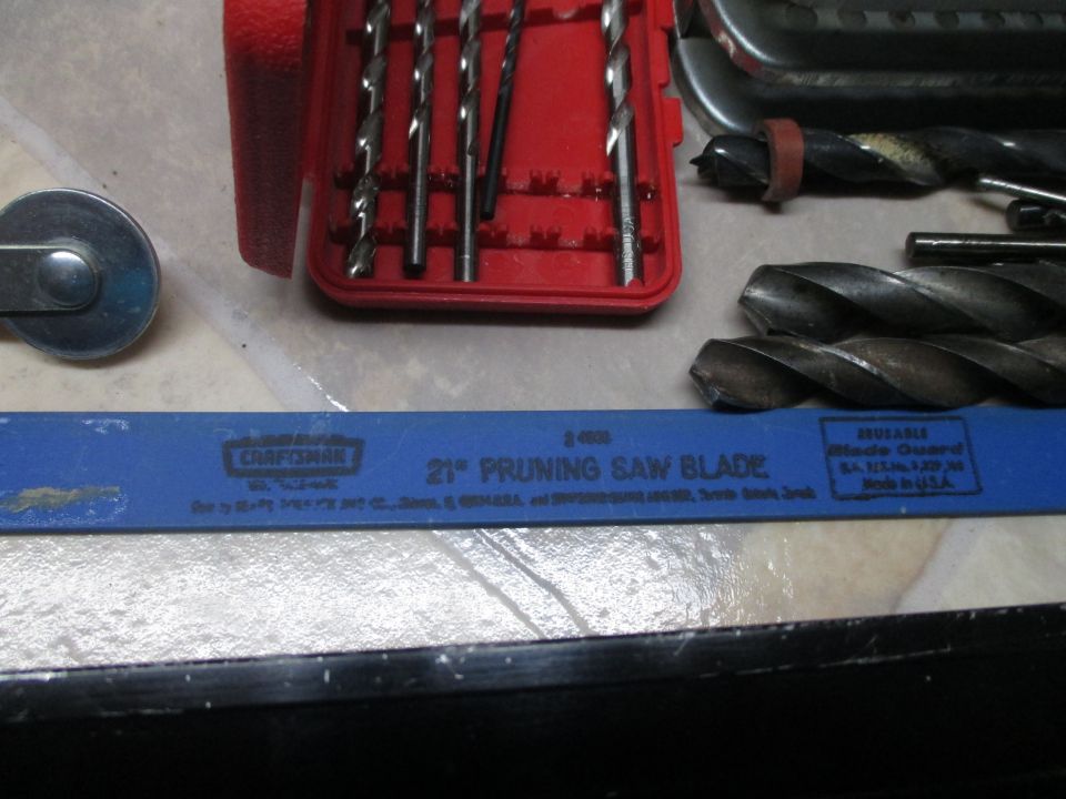 Red drill bit case with several bits, and a blue Craftsman 21" pruning saw blade