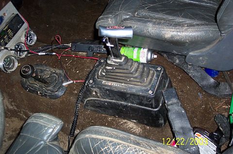 1978 Ford Bronco - The interior of a vehicle shows a floor-mounted shifter, a transfer case shifter, and various gauges, along with a can of lubricant.