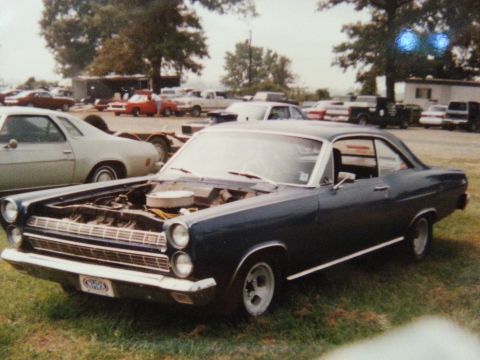 1967 Ford Mustang - A dark blue 1967 Mercury Cougar is parked on grass, its hood open, with several other vehicles visible in the background.
