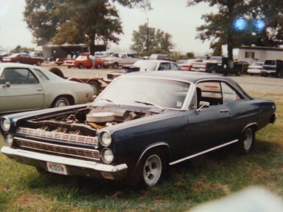 Dark blue 1967 Mercury Cougar with hood open, parked on grass with other cars in background
