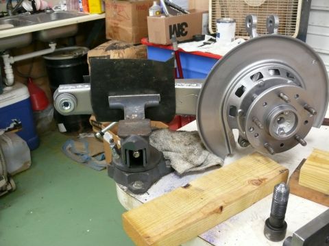 1976 Chevrolet Corvette - A car's brake rotor and hub assembly is secured in a vise, ready for work in a cluttered garage setting.