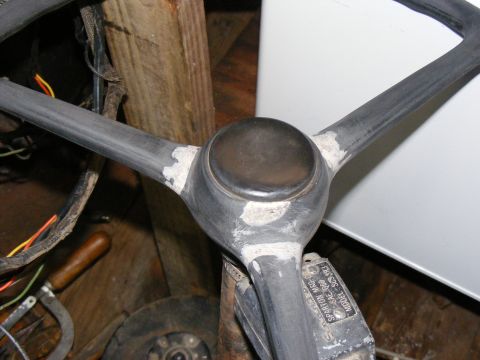Close-up of a three-spoke steering wheel with a dark center cap. Some white filler is visible on the spokes wh
