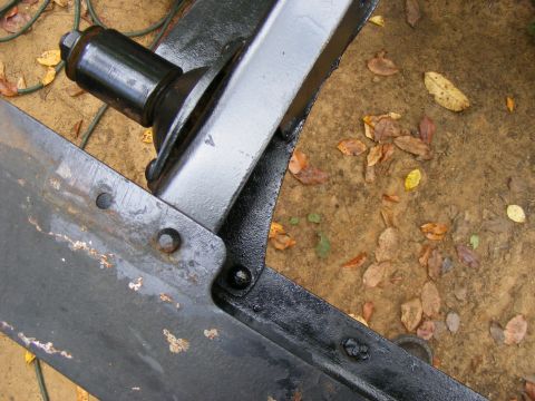 Black painted metal frame and suspension parts with rust spots, on dirt ground with fallen leaves