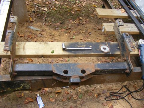 Trailer hitch assembly with a socket wrench, wire brush, and grinder. A tube of grease is on the ground