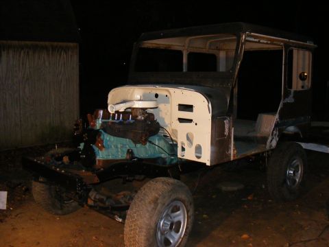 Unfinished SUV body, possibly a Jeep or Land Cruiser, with engine installed. Body is mostly bare metal and pri