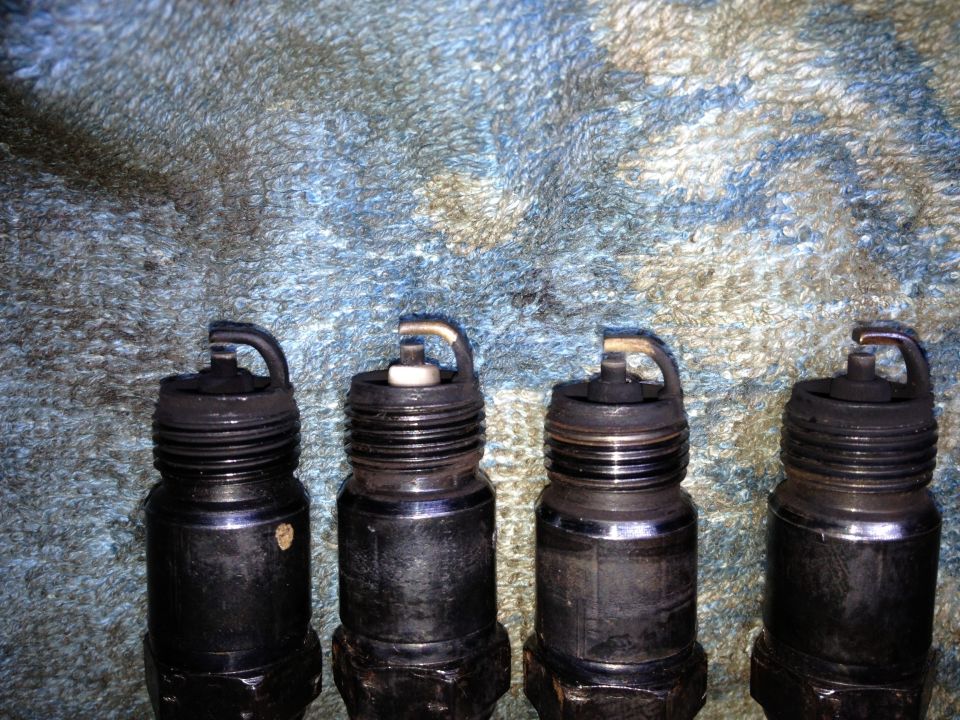 Four used spark plugs lined up on a textured surface