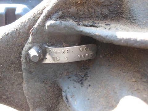 Metal identification tag with stamped numbers and letters on a dirty vehicle component