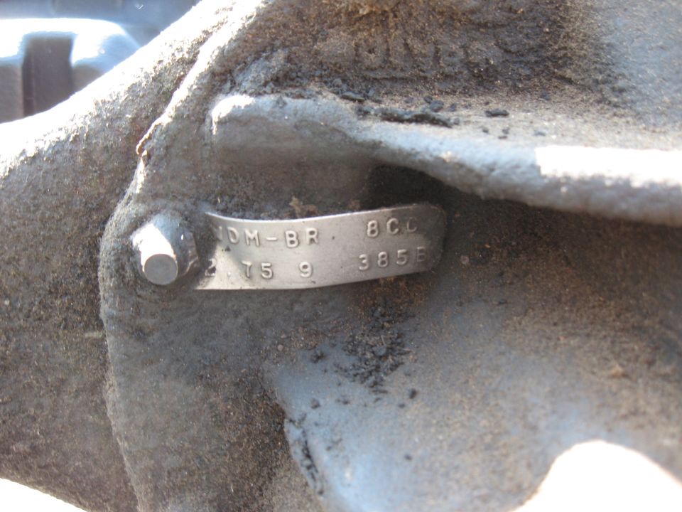 Metal identification tag with stamped numbers and letters on a dirty vehicle component