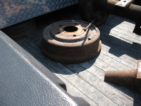 Rusty brake drum with a metal rod resting on it, sitting on a wooden surface
