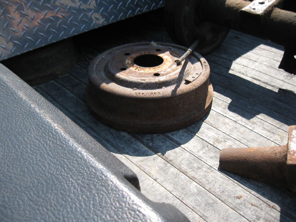 Rusty brake drum with a metal rod resting on it, sitting on a wooden surface