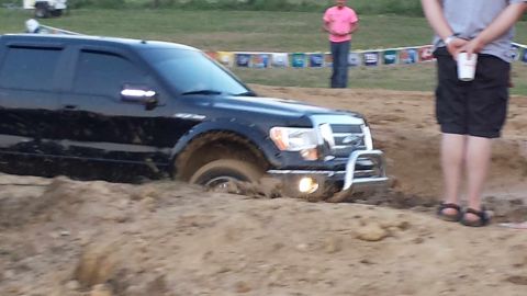 1987 Ford Bronco - A black Ford F-150 is stuck in a mud pit with its front end submerged.