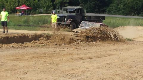 1987 Ford Bronco - Off-road vehicles navigate a muddy track, kicking up dirt and water.
