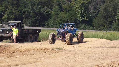 1987 Ford Bronco - A man stands by a large military truck while a custom off-road buggy sits nearby in a dirt lot.
