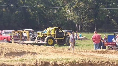 1987 Ford Bronco - A heavily modified yellow truck with a roll cage sits on display at an outdoor event.
