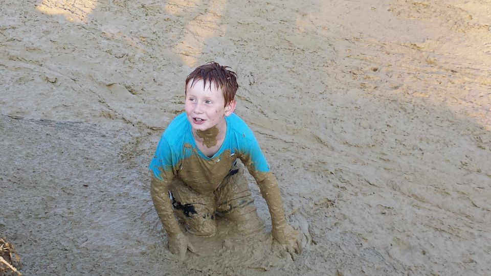 Boy in blue shirt covered in mud, sitting in a muddy area