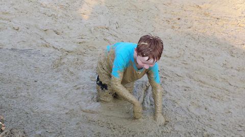 1987 Ford Bronco - A child is covered head to toe in mud while crawling through a muddy area.