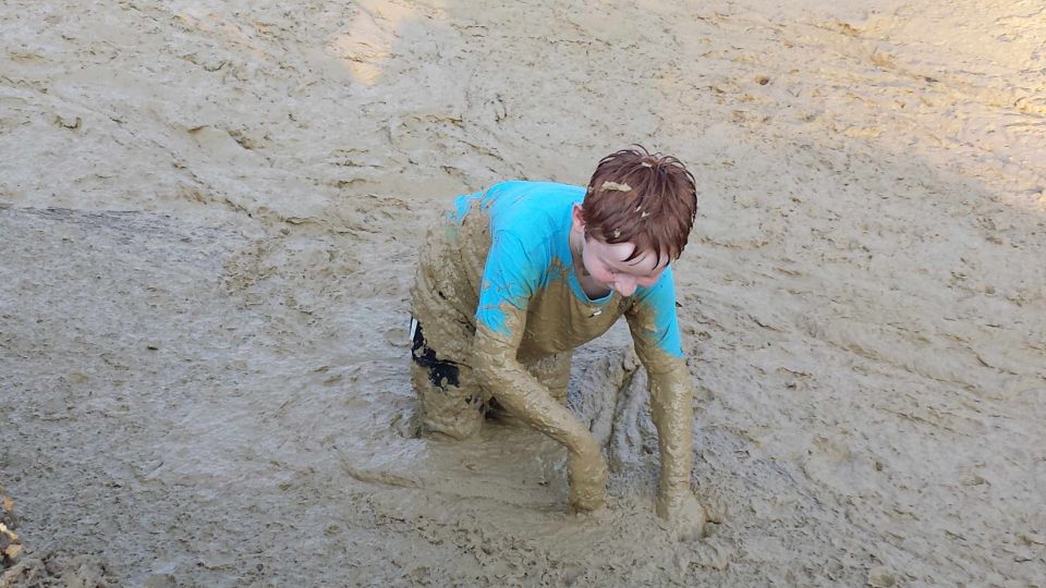 Child in blue shirt and shorts crawling through thick mud