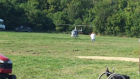 1987 Ford Bronco - A helicopter sits in a grassy field with a person walking towards it and a pickup truck in the background.