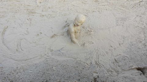 1987 Ford Bronco - A person is submerged in thick mud, with only their head and upper torso visible.