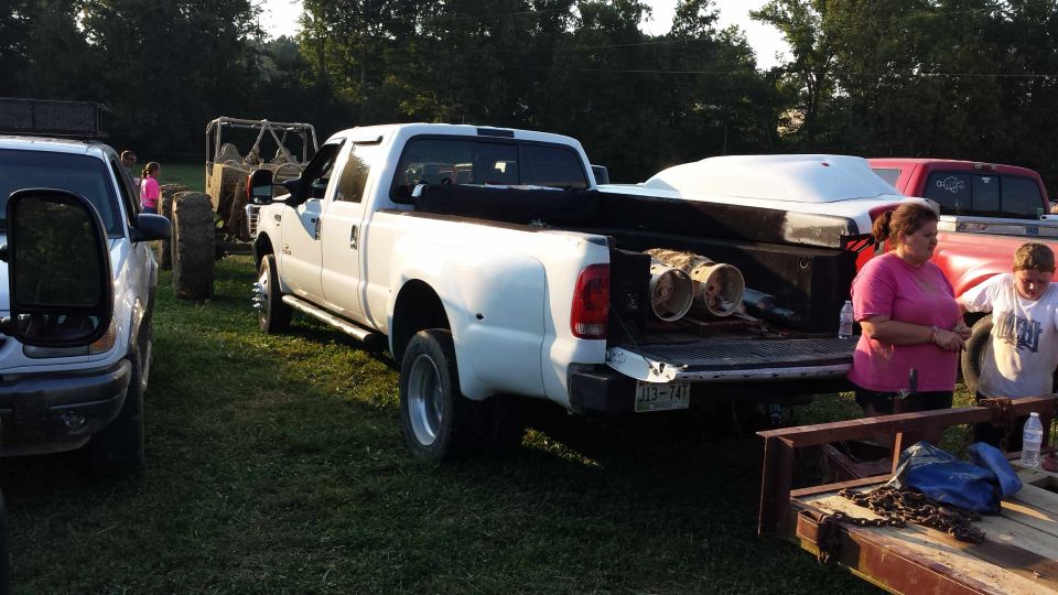 White pickup truck with its tailgate down, carrying a white cover and two cylindrical objects