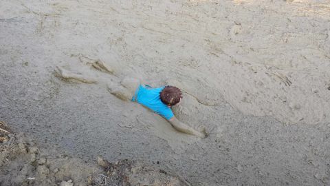 1987 Ford Bronco - A person wearing a blue shirt is stuck in thick mud, with the Supermotors logo visible in the lower right corner.