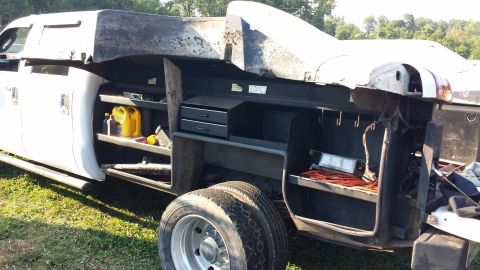 1987 Ford Bronco - The side of a service truck bed is shown, open shelves with various items and dual rear wheels.