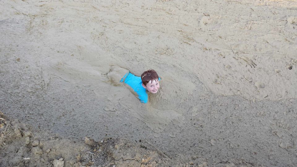 Child in blue shirt stuck in mud, smiling at the camera