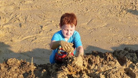 1987 Ford Bronco - A young boy is covered in mud while playing with a toy truck in a muddy area.